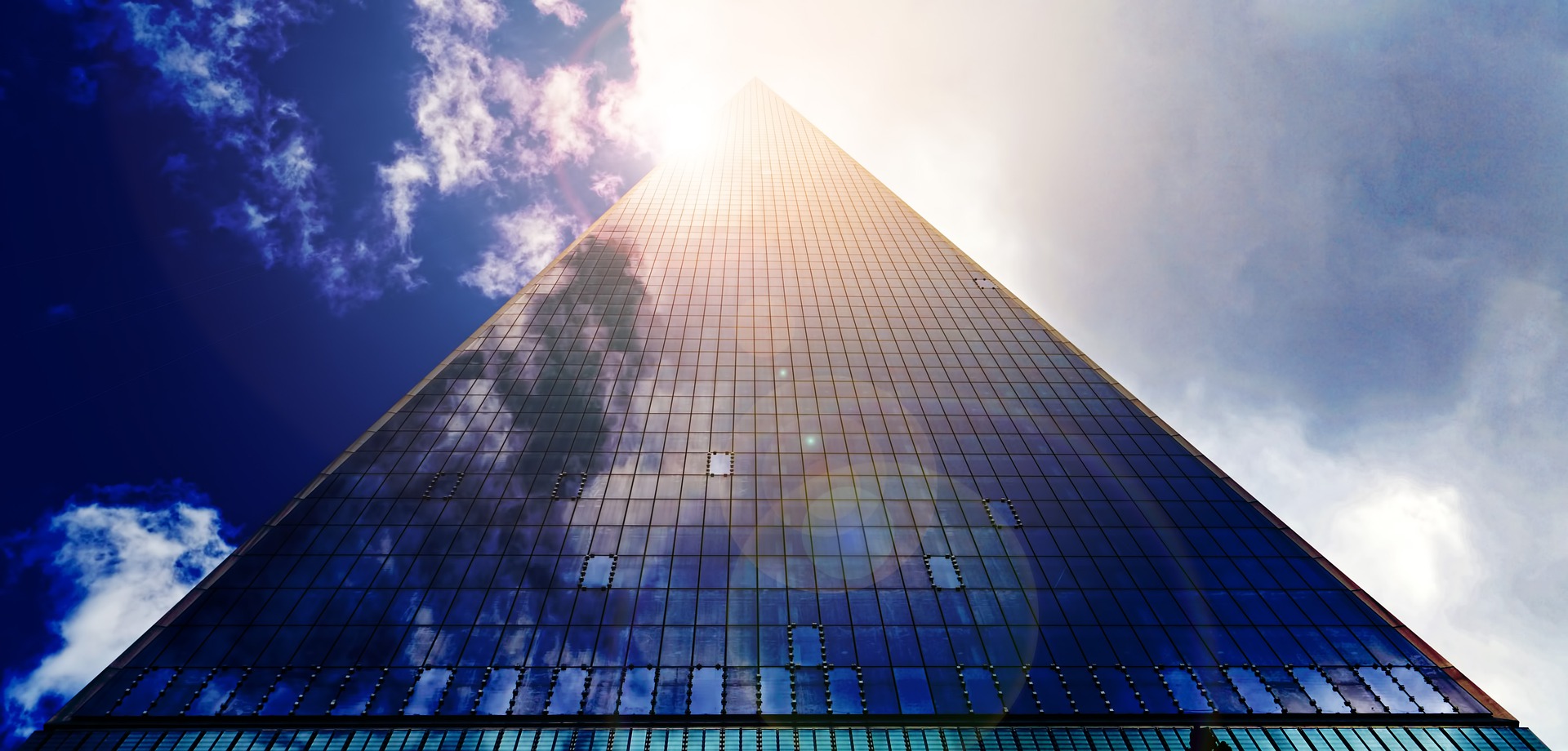 A skyscraper building fading into a partly cloudy sky