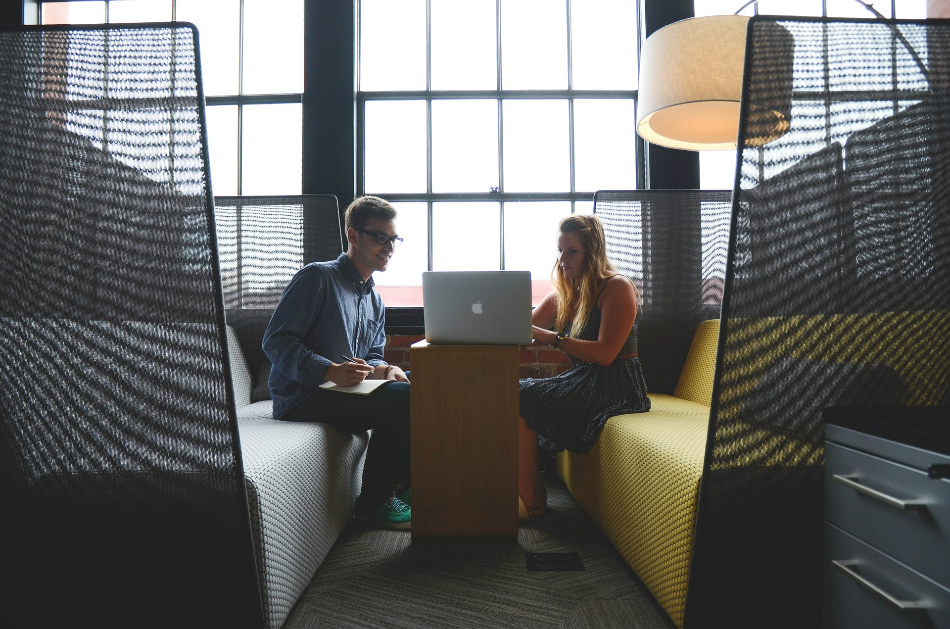 A man and woman sit behind a laptop inside a booth