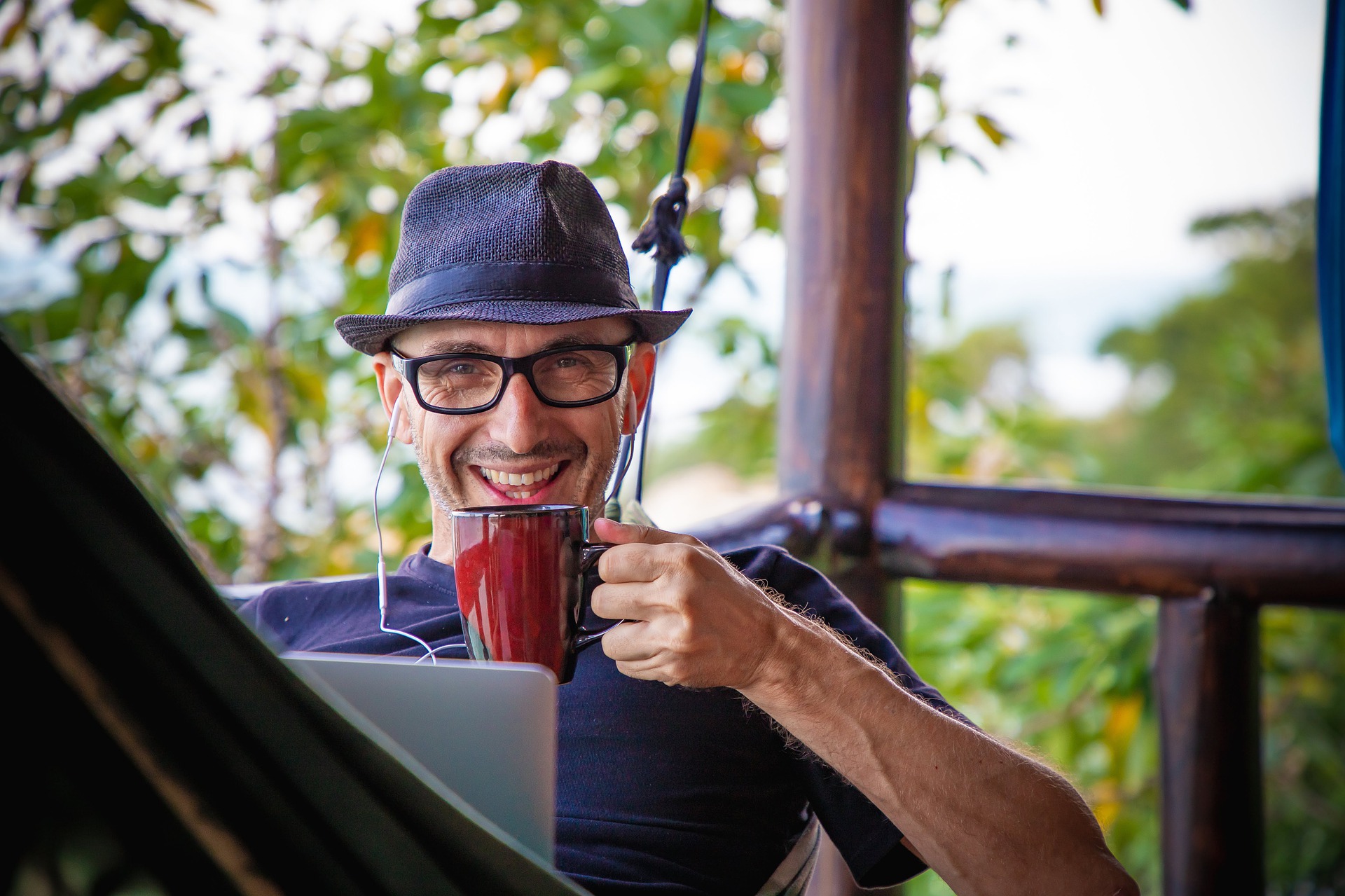 A happy man laying in a hammock drinking coffee