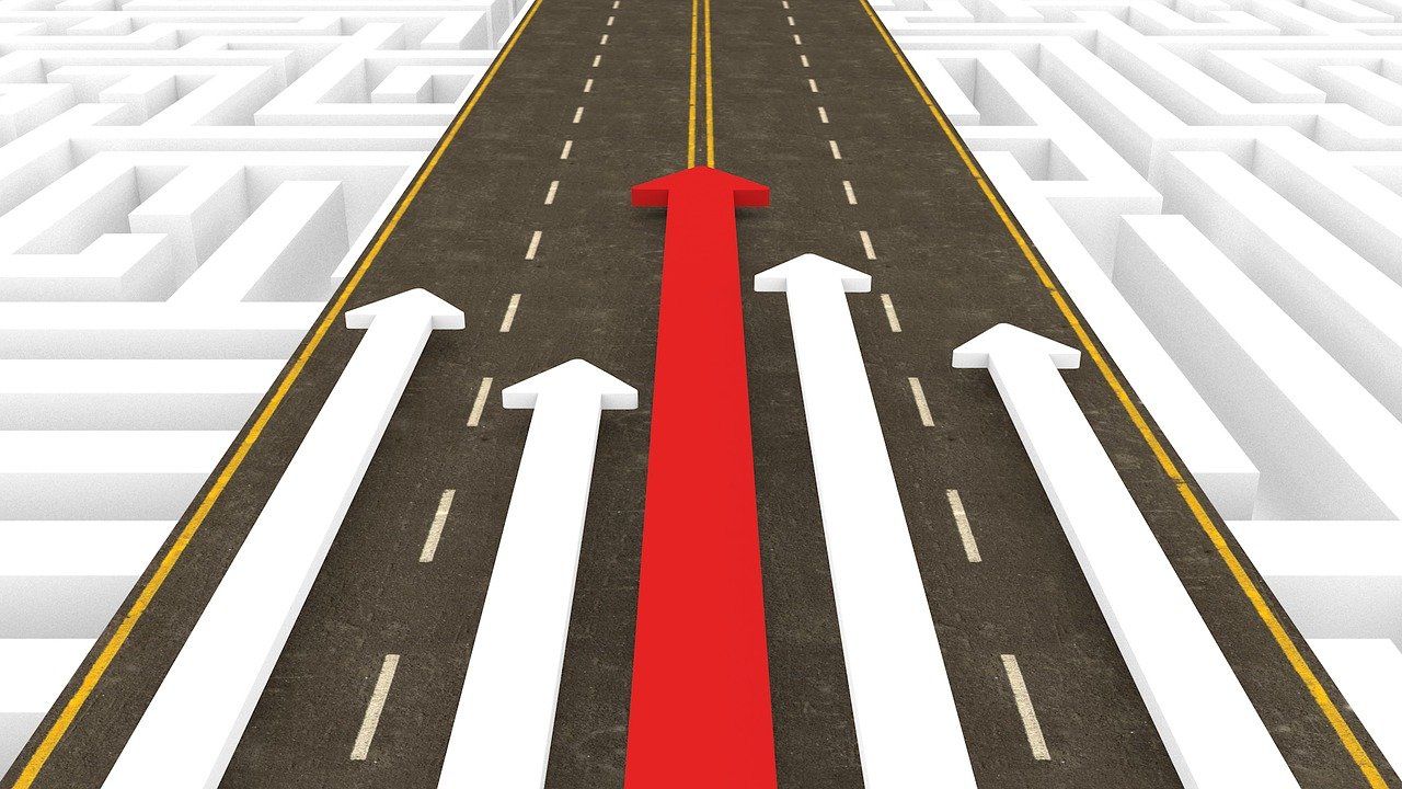 A red arrow surrounded by 4 white arrows moving down a road.