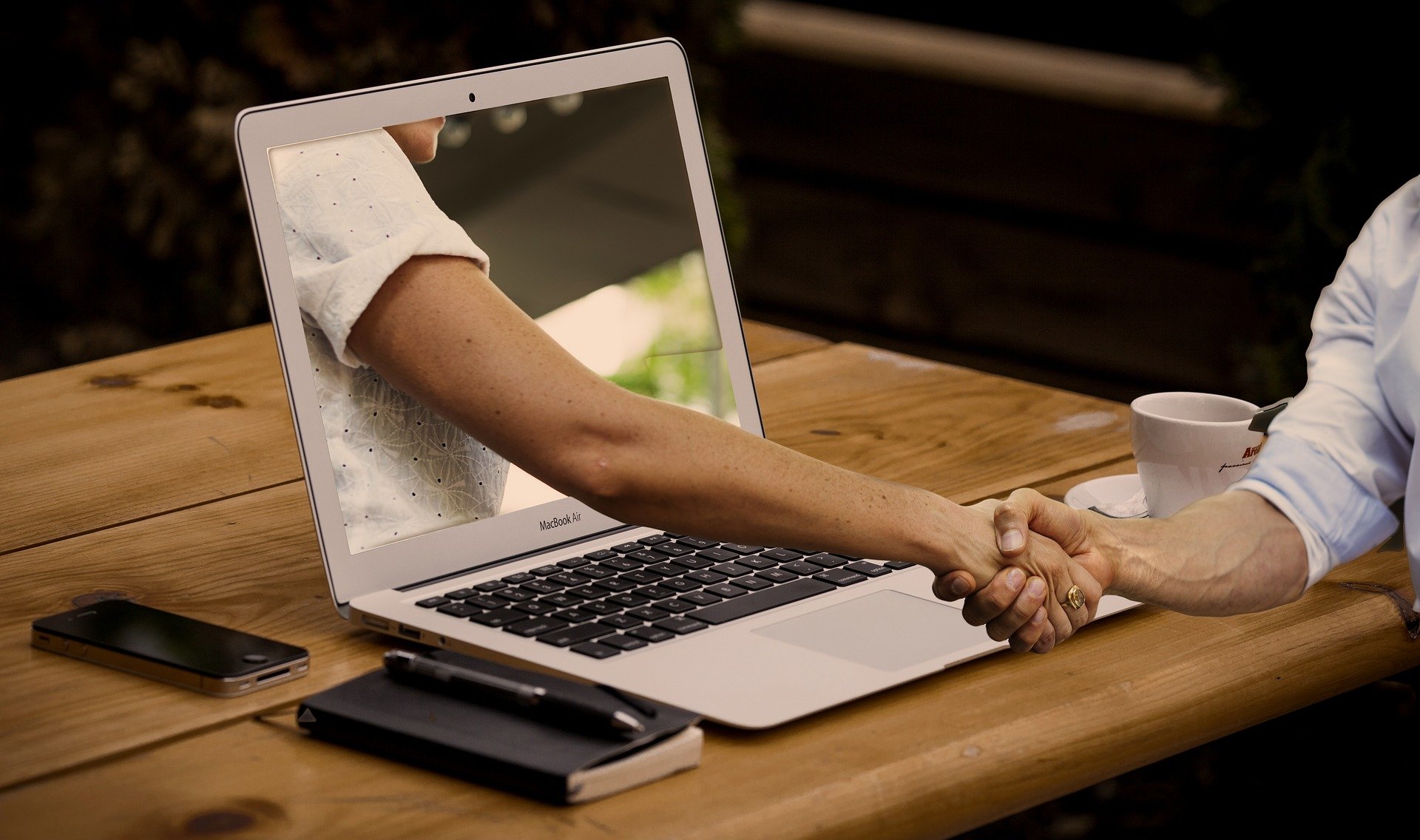 Two people shaking hands through a laptop screen.