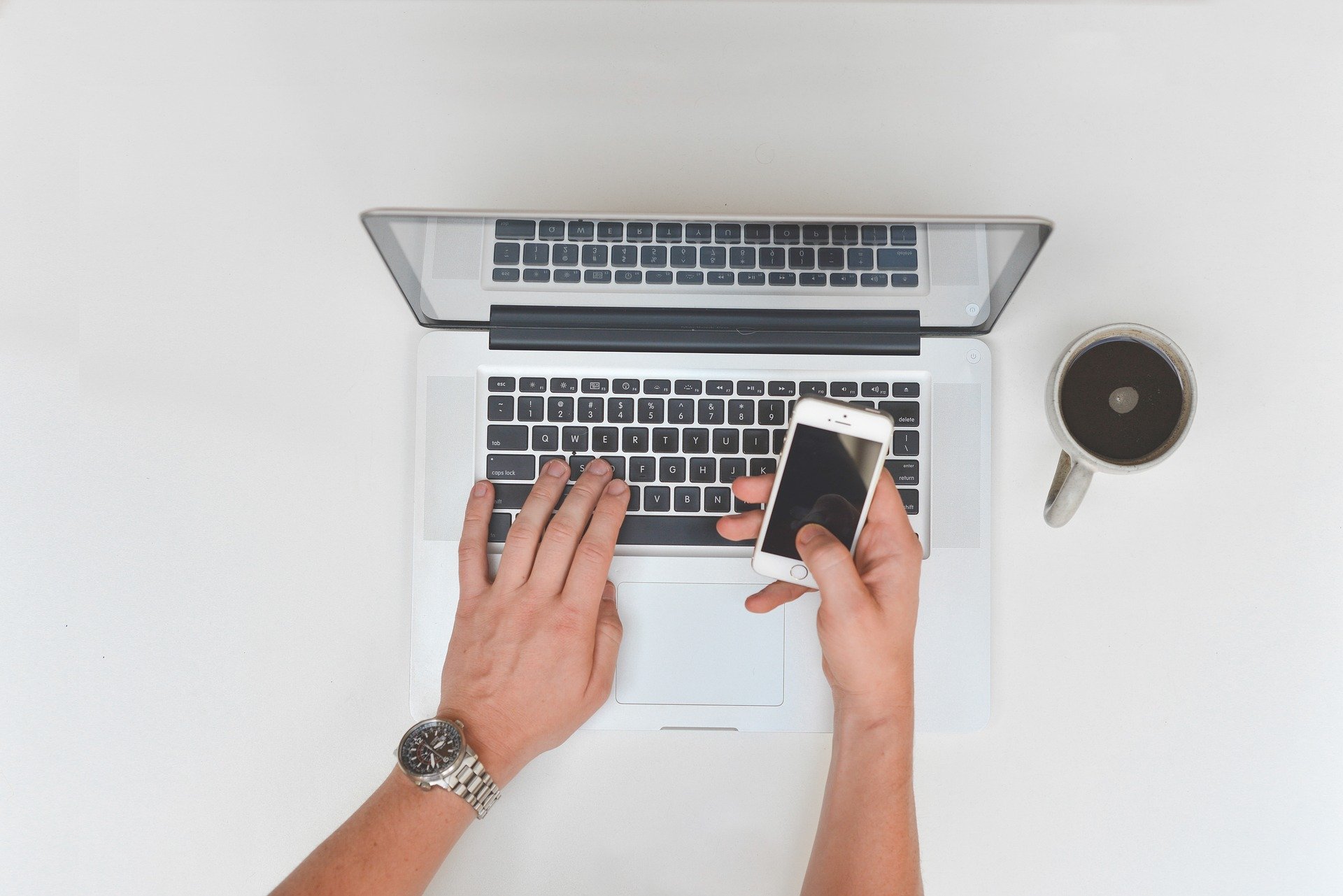 A person working on a laptop holding a smart phone.