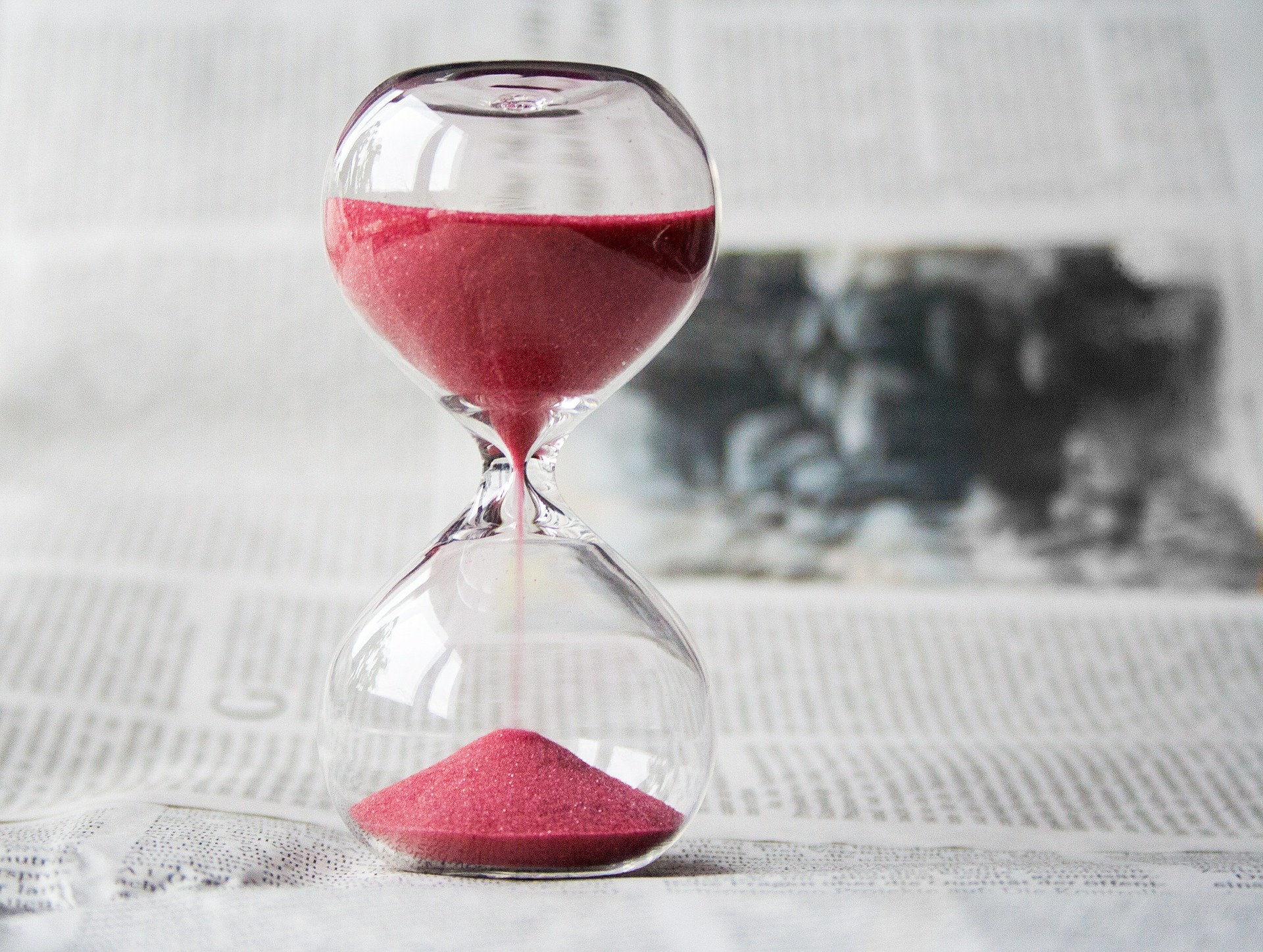 An hour glass with red sand sitting on a book.