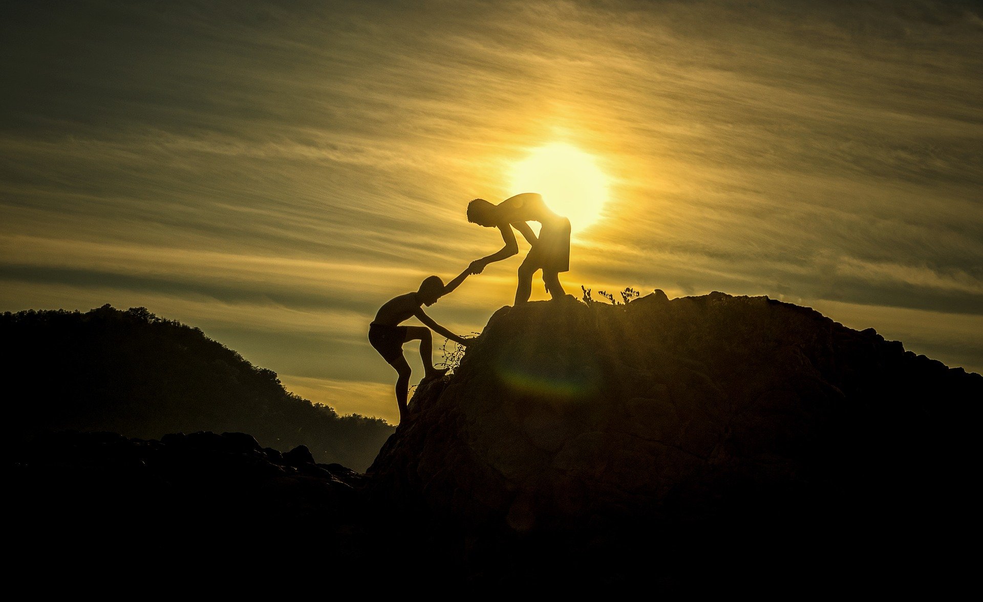 A picture of two people climbing up a mountain with one person helping the other.