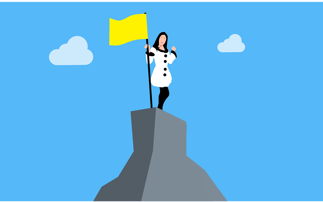 A person dressed in business attire standing on top of a mountain holding a yellow flag.