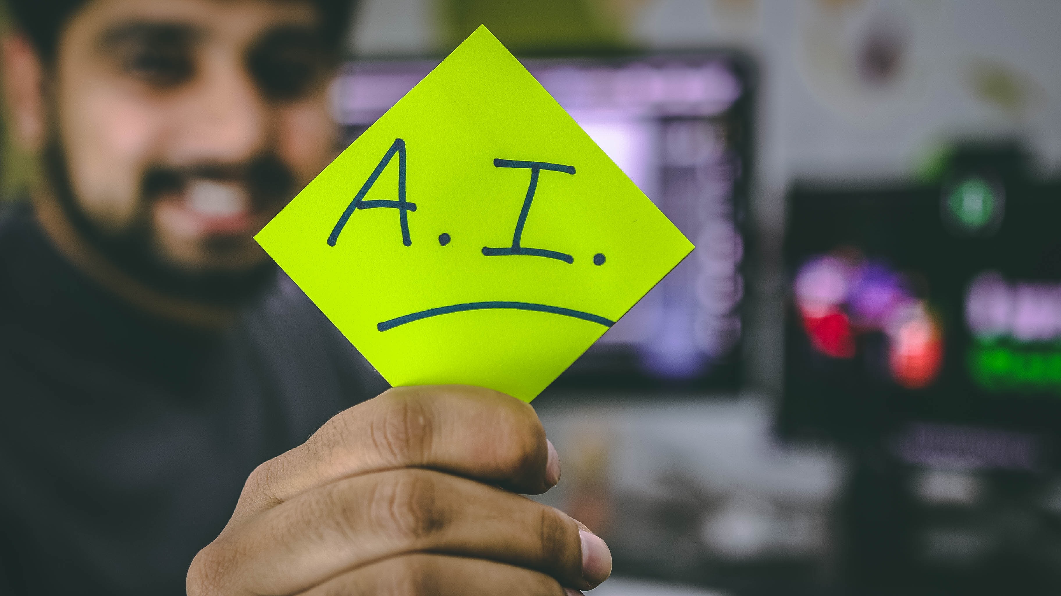 A blurred image of a man holding a sticky note that has A.I. written on it.