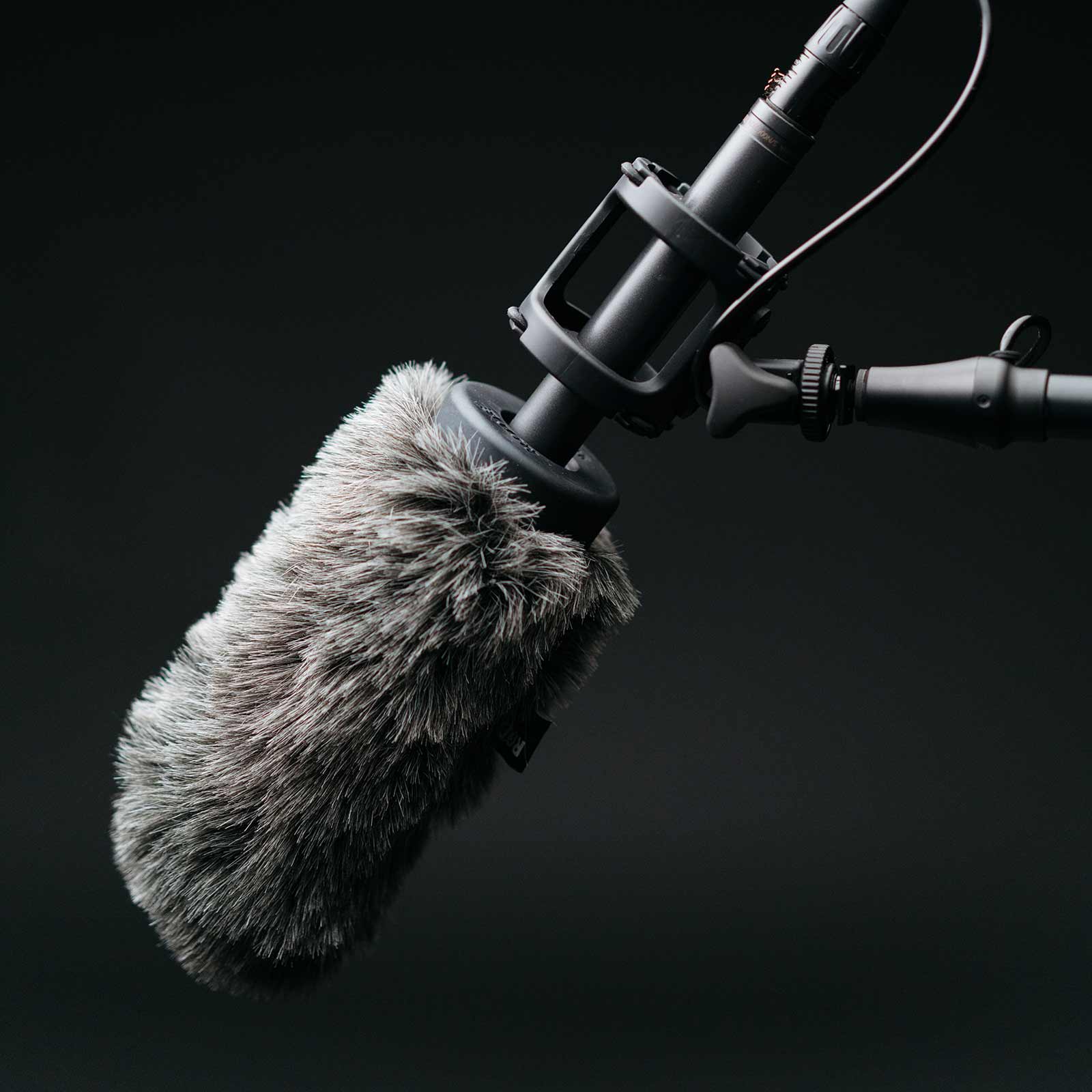 A gray studio microphone is angled down with a black backdrop behind it
