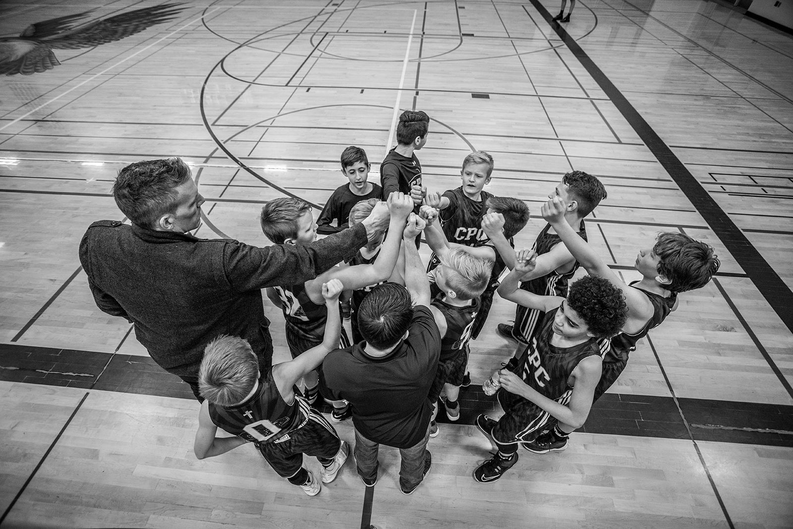 A basketball coach puts hands together with team in black and white