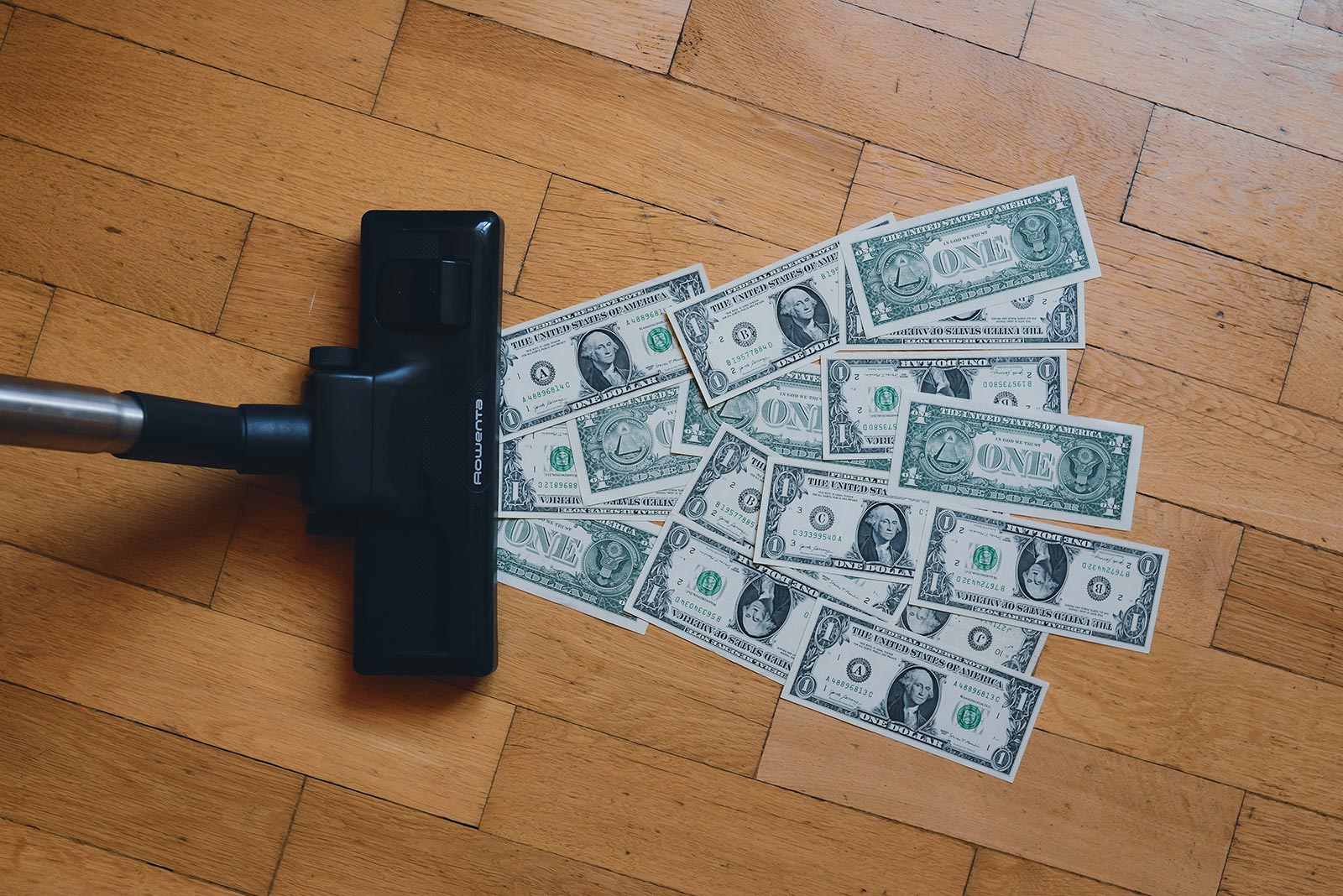 A vacuum sucks up a pile of one dollar bills off the floor.