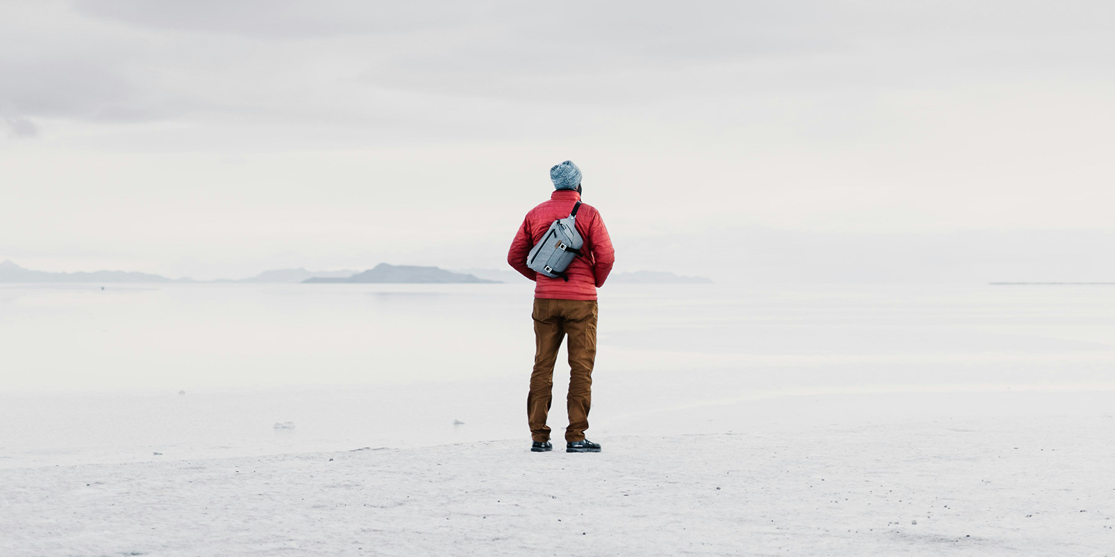 A man standing in a red jacket looks out over a tundra landscape.