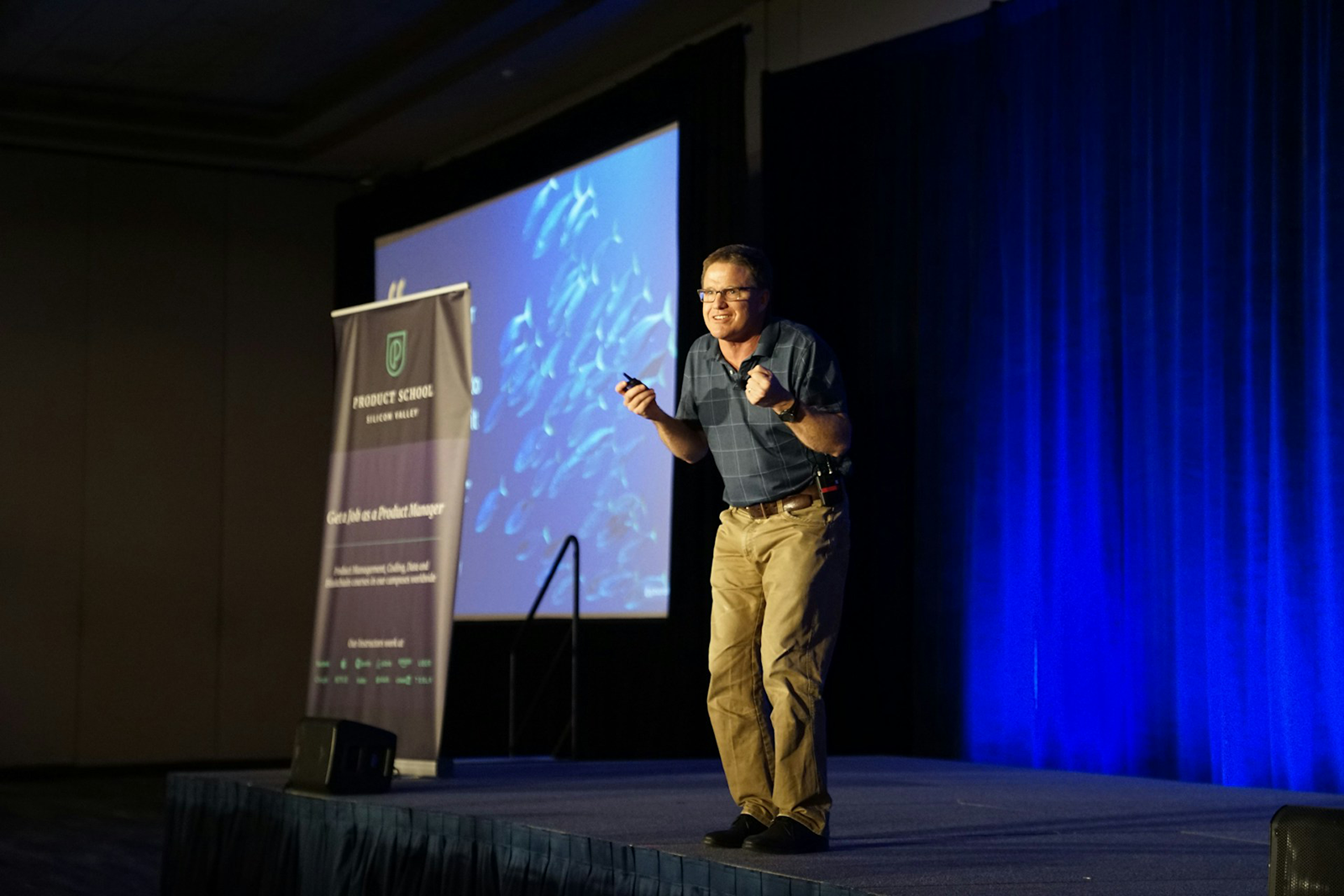 A man stands on a stage giving a presentation with a screen behind him.