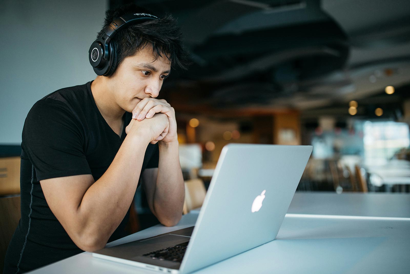 A man looks at his laptop wearing black headphones.
