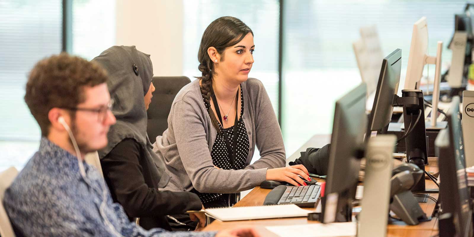 Three people sit at their computers working.