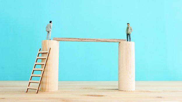 Two people stand on blocks with another block between them.