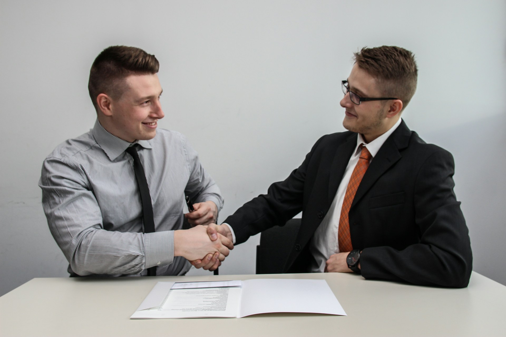 Two men facing each other while shaking hands and smiling.