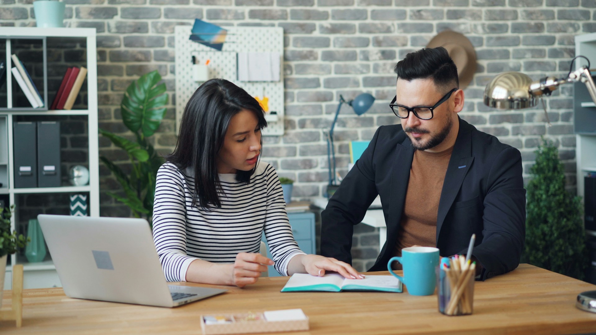 A man and a woman sitting at a table looking at a laptop.