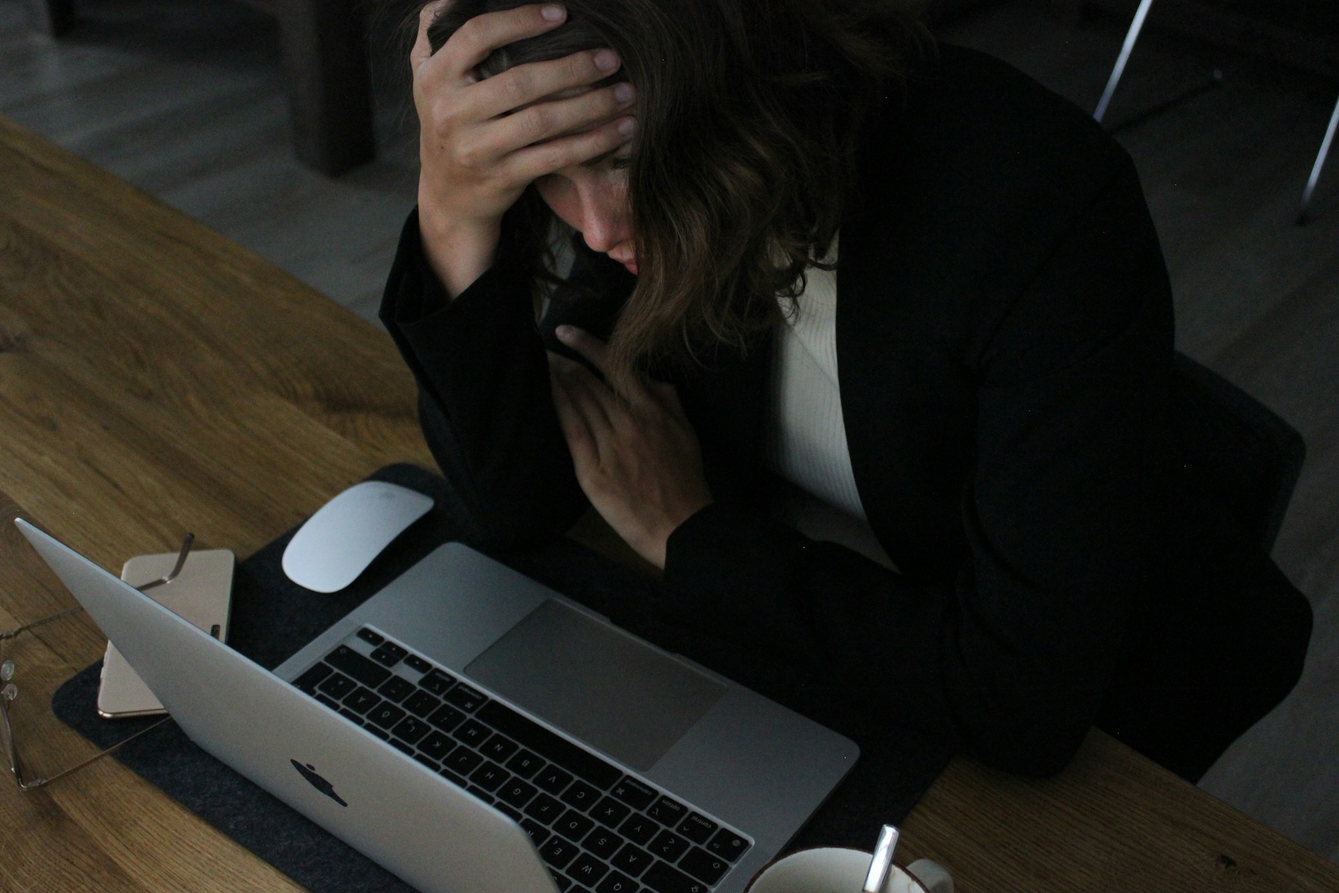 A woman sitting in front of a laptop with her head in her hand.